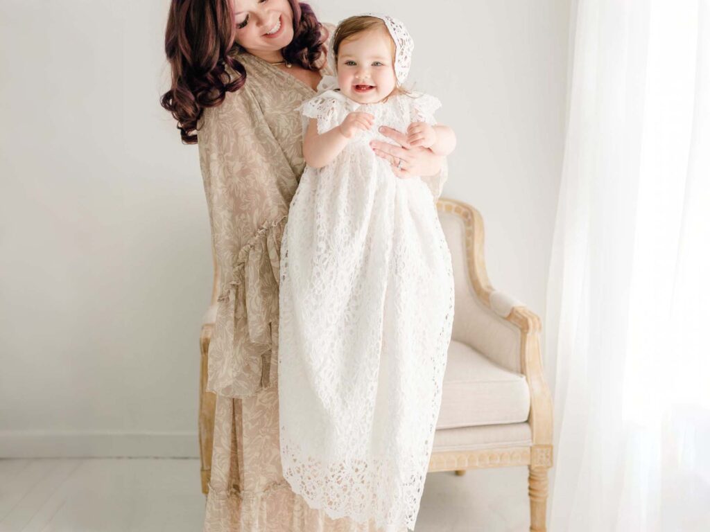 Mother holding a baby girl dressed in a white lace baptism dress and bonnet