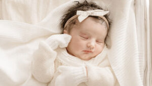 Newborn baby in white knit romper and mittens