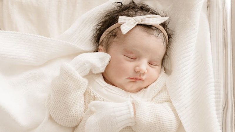 Newborn baby in white knit romper and mittens